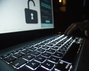 Teclado de computadora iluminado en un ambiente oscuro, con fondo de cerraduras de seguridad. Las teclas muestran desgaste y se destacan con sombras marcadas.