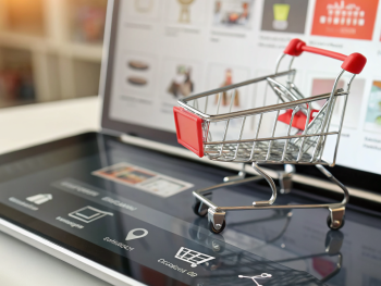 Primer plano de la interfaz de un carrito de compras digital en un dispositivo moderno, con botones destacados para agregar productos y un área de pago simplificada. Al fondo, miniaturas de productos desenfocadas y un icono de reloj de arena en la pantalla, sugiriendo facilidad y rapidez en la experiencia de compra.